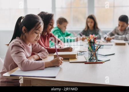 Asian Schoolgirl Taking Notes Learning Sitting In Modern Classroom Stock Photo