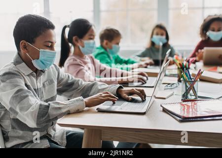 Black Schoolboy Using Laptop Having Class In Modern Classroom Stock Photo