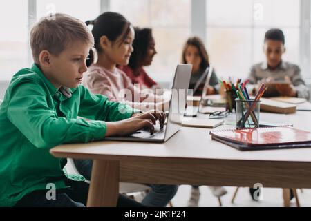Boy Using Laptop Sitting With Multiethnic Classmates In Modern Classroom Stock Photo