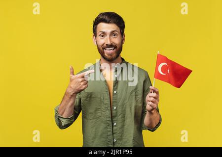 Happy man holding and pointing at China flag in his hand, posing and smiling at camera over yellow background Stock Photo