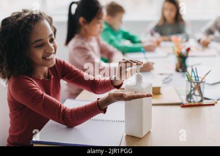 Black Schoolgirl Applying Sanitizer Disinfecting Hands During Class In Classroom Stock Photo