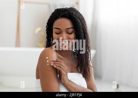 Body Treatments. Attractive Black Lady Applying Moisturising Cream On Shoulder Stock Photo