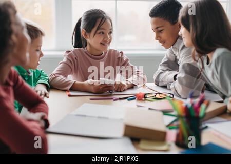 Happy Multicultural School Children Using Phone During Break In Classroom Stock Photo