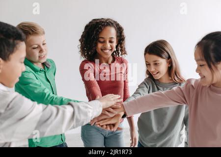 Cheerful Kids Putting Hands Together Standing In Circle Posing Indoors Stock Photo