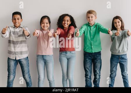Happy Multiethnic Kids Gesturing Thumbs Up Posing Standing Indoor Stock Photo