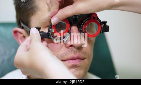close-up, portrait of Handsome young man trying on blue sunglasses at optical store, optician retail store. in glasses of spectacles is reflected the showcase of optics with glasses. High quality photo Stock Photo