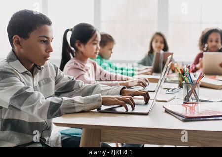 Side View Of African American Schoolboy Using Laptop In Classroom Stock Photo