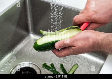 Peeling a cucumber for eating over the sink Stock Photo
