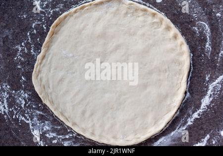 Rolled out pizza dough on floured slate surface, photographed overhead Stock Photo