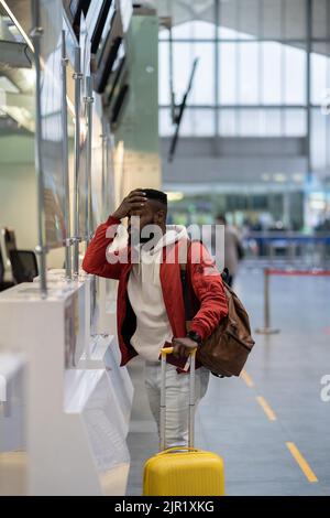 Upset African man standing at check-in counter in airport, being sad about moving away Stock Photo