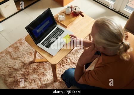 Senior man writing e-mail password on yellow sticky note Stock Photo
