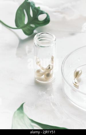 Serum capsules for healthy skin. Blurred background, glass jar with the capsules and green monstera leaf Stock Photo