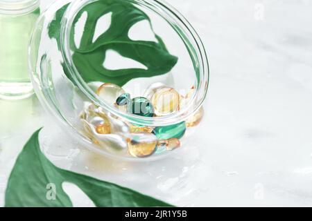 Serum capsules for healthy skin. Blurred background, glass jar with the capsules and green monstera leaf Stock Photo