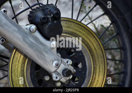 Detail of a disc brake with caliper and fork mounted on a spoked wheel of a vintage motorcycle. Stock Photo