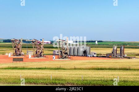 Oil wells with working puumpjacks, storage tanks at an oil field near Dickinson, North Dakota Stock Photo