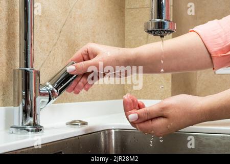The concept of lack of tap water. The faucet has no running water. Drops of water drip from faucet in human palm above metal kitchen sink Stock Photo