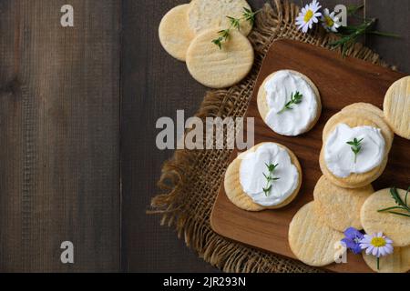 Delicious crackers with cream cheese and rosemary on top. Cookies with cream cheese on wood background and copy space. snack food concept Stock Photo