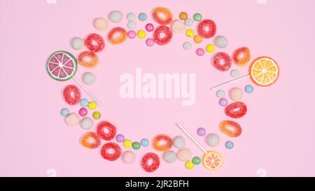 sweet candies and jelly beans make copy space frame on pastel pink background. Flat lay Stock Photo