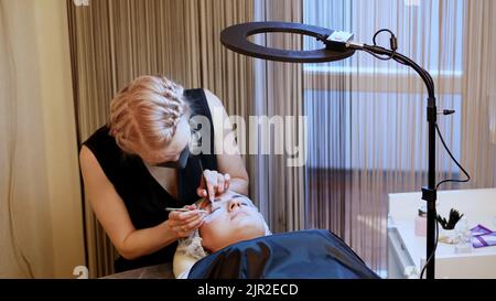 beauty saloon. procedure for eyelash extension. The master in the bandage on the face, glues each cilium with special glue, works by means of two tweezers. High quality photo Stock Photo