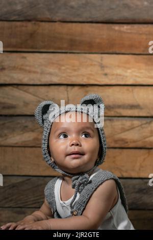 vertical photo of a beautiful latin baby girl with brown skin, wearing overalls and a cap with mouse ears, crocheted with the crochet technique, on a Stock Photo
