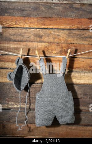 vertical detail shot of baby clothes, hanging from a clothesline with wooden hooks, overalls and hat. clothes are drying in the shade. copy space. cle Stock Photo