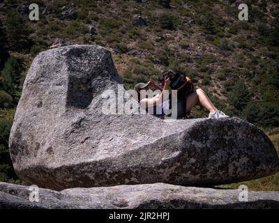 Female dog owner playing with her chocolate labrador retriever  on a granite boulder with sofa shape. Stock Photo