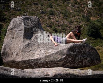 Female dog owner resting on a granite boulder with sofa shape and chocolate labrador retriever looking at camera. Stock Photo