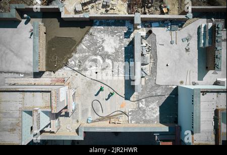 Top view of construction site with workers, building materials, brick walls and floor screed process. Floor screeding contractors walking down newly build apartment building with concrete floor. Stock Photo