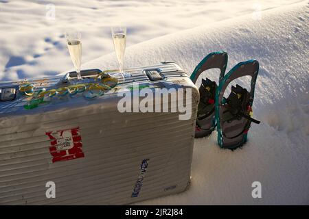 A closeup of snow shoes and two glasses of champagne on a silver suitcase in fluffy white snow Stock Photo