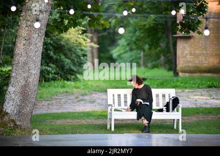 A woman sits on a park bench and reads a book. Stock Photo