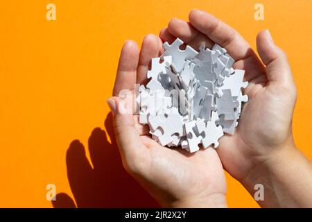 White puzzle pieces in the hands on the orange background. Concept of board game. Stock Photo