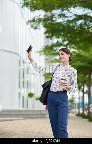 Smiling young business woman waving somebody with phone in her hand Stock Photo