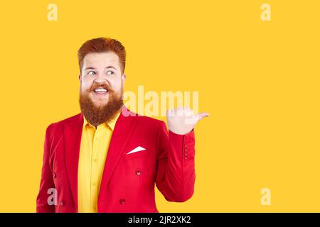 Funny Caucasian man with beard and moustache showing finger at copy space stands on yellow studio Stock Photo