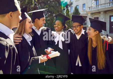 Happy multiracial university graduates walking, talking, laughing and hugging together outdoors. Stock Photo
