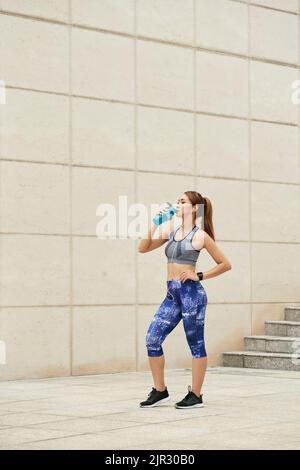 Tirsty fit young woman drinking fresh water after intense training outdoors Stock Photo