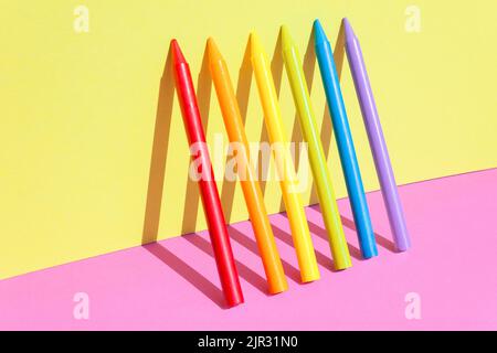 Creative back to school concept. Multiple colorful wax crayons isolated on the pink and yellow color background. Copy space. Stock Photo