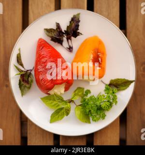 Red and yellow bell peppers stuffed with cheese garnished with basil and parsley top view Stock Photo