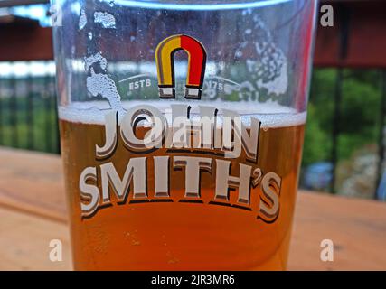 John Smiths, Magnet Ales, pint glass, ESTB 1758, half-full of beer, Llangollen, North Wales, UK - the highest selling bitter in the United Kingdom Stock Photo
