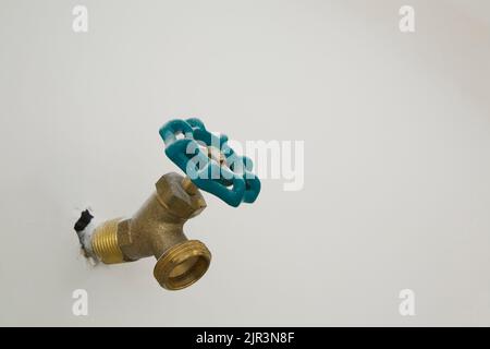 Brass water faucet sticking out of white gypsum wall inside garage of residential home. Stock Photo