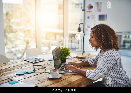 Shes the best in the creative buz. a woman using her laptop on a wooden table. Stock Photo