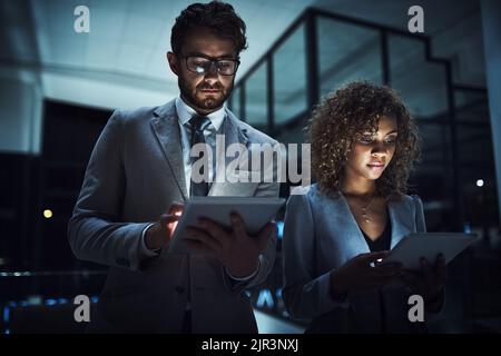 Dedication keeps them performing, no matter the hour. a group of businesspeople working late on digital tablets in an office. Stock Photo