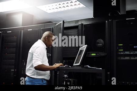 Skilled in all things IT. an IT technician using a computer while working in the server room of a data center. Stock Photo