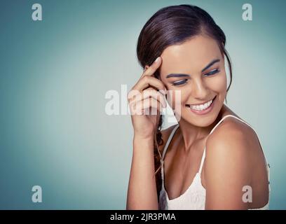 She is so stunning yet still so shy. Studio shot of a beautiful young woman posing against a green background. Stock Photo