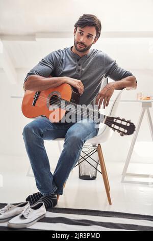 He first thinks deeply on what to play. a handsome young man practising guitar at home. Stock Photo