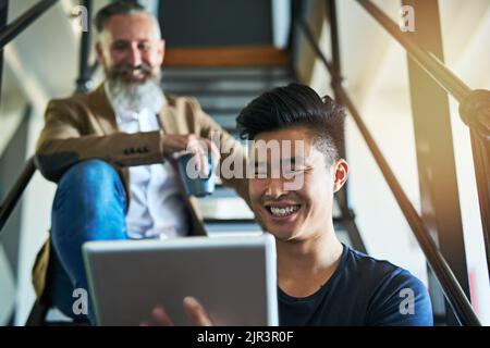 Digital collaborations. two businessmen using a digital tablet while sitting on a staircase in an office. Stock Photo