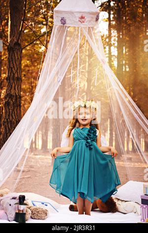 I am the fairest of them all. a happy little girl looking at the camera and holding her beautiful dress wile standing outside in the woods. Stock Photo