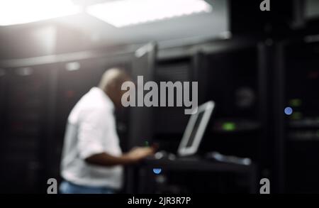 Keeping your computer systems up to date. an IT technician using a computer while working in the server room of a data center. Stock Photo