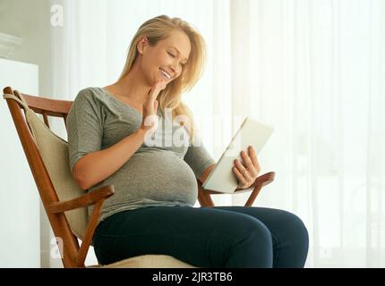 Connecting with other expectant parents. a pregnant woman using her digital tablet while sitting on a rocking chair. Stock Photo