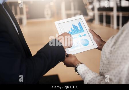 Finding ways to push their profits up. Closeup shot of two unrecognisable businesspeople analysing graphs on a digital tablet in an office. Stock Photo