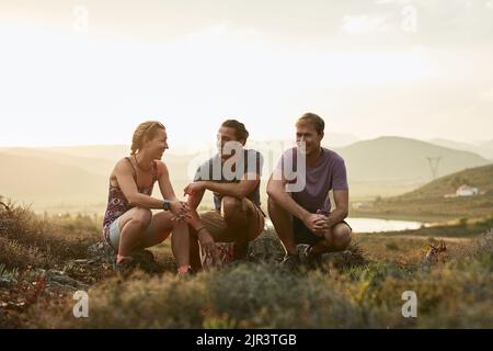 Great company in the grand outdoors. three happy young hikers taking a break on a mountain trail. Stock Photo
